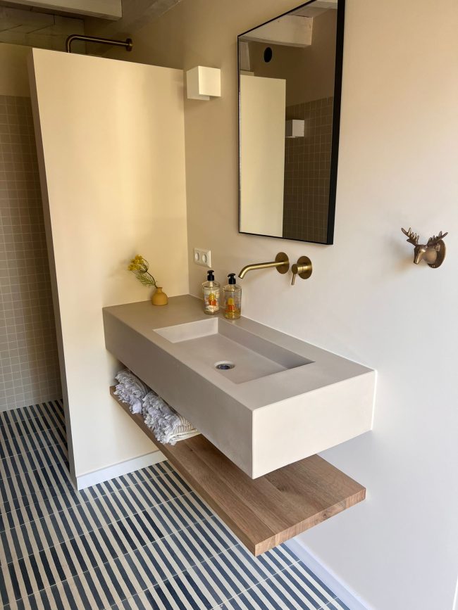 Wastafel van beton zwevend met kraan uit de muur en eiken legplank