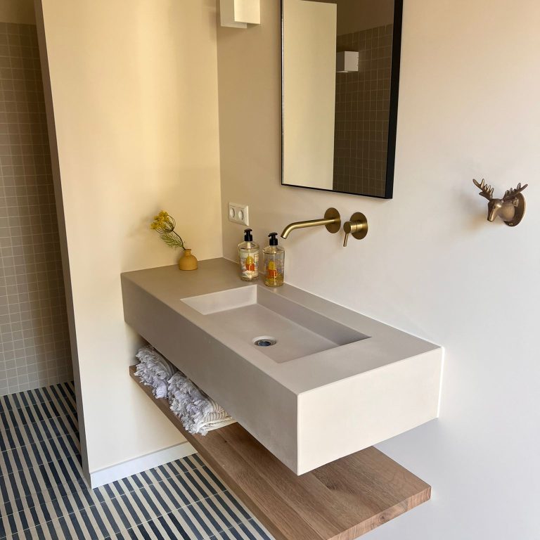 Wastafel van beton zwevend met kraan uit de muur en eiken legplank